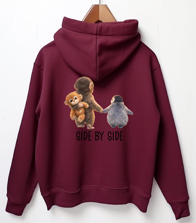 May include: A maroon hoodie with a hood and long sleeves. The back features a graphic of a monkey holding a smaller monkey and a penguin, with the text "SIDE BY SIDE" below the image.