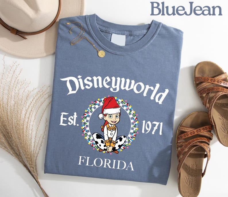 May include: A blue t-shirt with the text "Disneyworld Est. 1971 Florida" and a cartoon character wearing a Santa hat. The shirt is paired with brown sandals and a beige hat.