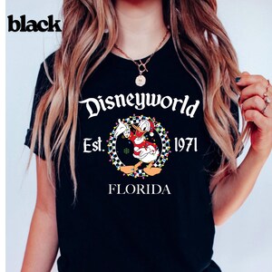 May include: Black t-shirt with a Disneyworld graphic. The graphic features Donald Duck in a Santa outfit, surrounded by a wreath and the text "Disneyworld Est. 1971 Florida". The word "black" is printed in the upper left corner.