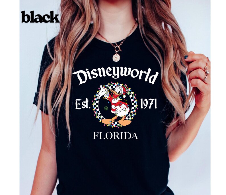 May include: Black t-shirt with a Disneyworld graphic. The graphic features Donald Duck in a Santa outfit, surrounded by a wreath and the text "Disneyworld Est. 1971 Florida". The word "black" is printed in the upper left corner.