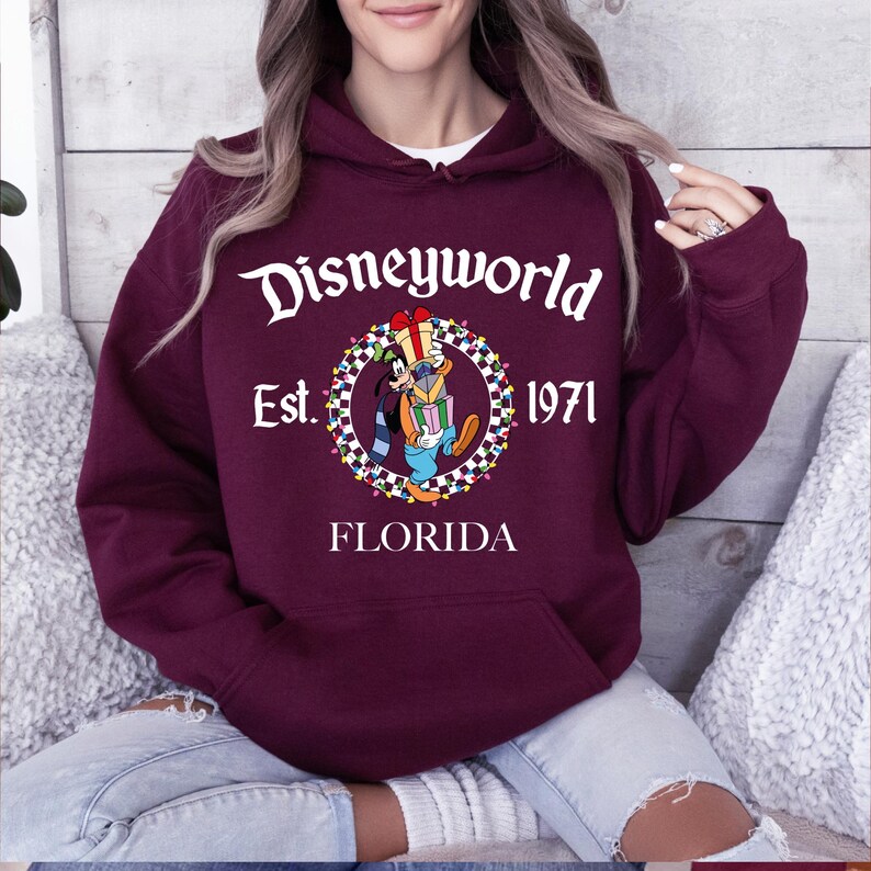 Pu&ograve; includere: Felpa con cappuccio bordeaux con grafica frontale con la scritta "Disneyworld Est. 1971 FLORIDA" e un'immagine a cartoni animati di Pippo che tiene dei regali. La felpa ha una tasca a marsupio e un cappuccio con coulisse.