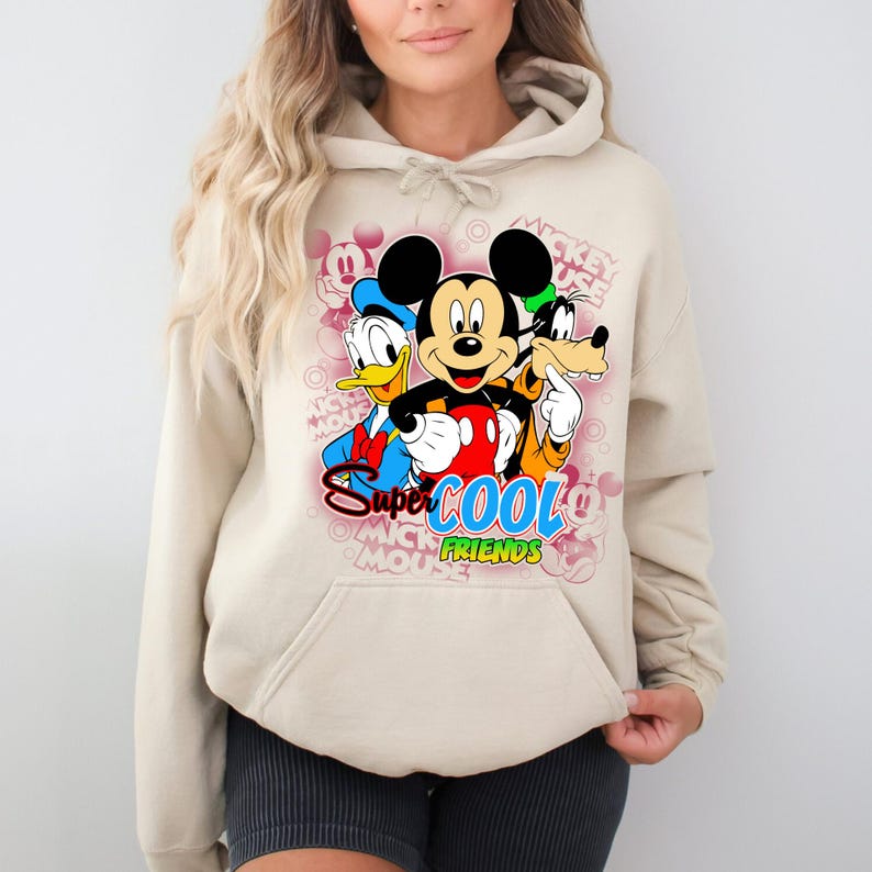 Puede incluir: Sudadera con capucha beige con un gr&aacute;fico colorido de Mickey Mouse, el Pato Donald y Goofy. El gr&aacute;fico incluye el texto "Super Cool Friends". La sudadera tiene un bolsillo delantero y mangas largas.