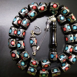 Könnte beinhalten: Eine schwarze Gebetskette mit silbernen Akzenten und roten und blauen Akzenten. Die Perlen sind rund und haben ein gepunktetes Muster. Die Kette ist auf einer silbernen Kette aufgefädelt und hat einen silbernen Quasten.