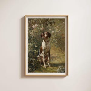 Op de afbeelding: Een ingelijste print van een hond die in een tuin zit. De hond heeft bruine en witte vlekken en draagt een halsband. De achtergrond toont weelderig groen en zachtroze bloemen, met een pad.