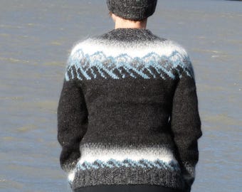 May include: A long-sleeve knit sweater and matching beanie featuring a dark charcoal gray base with horizontal bands of white and light blue mountain-inspired patterns across the chest, shoulders, and the lower hem of the sweater and beanie.