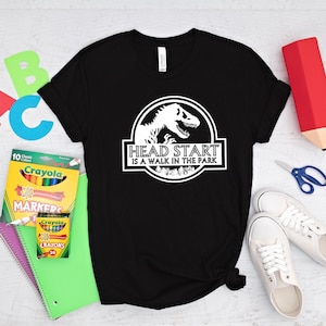 May include: Black t-shirt with a white dinosaur graphic and the text "Head Start is a walk in the park".