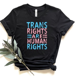 May include: Black t-shirt with the text "TRANS RIGHTS ARE HUMAN RIGHTS" in blue and pink lettering.
