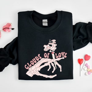 May include: Black sweatshirt with a pink skeleton hand holding a lit joint with pink smoke that says "Clouds of Love" in pink letters.