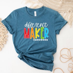 May include: Teal blue t-shirt with the text "difference maker" in rainbow colors and the hashtag "#teacher" in black.