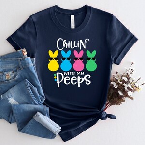 May include: Navy blue t-shirt with a graphic of three yellow, blue, and pink marshmallow peeps wearing sunglasses. The text "Chillin' with my Peeps" is printed below the peeps.