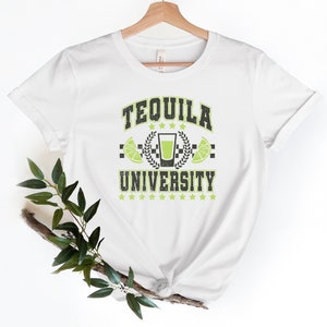 May include: White t-shirt with a green and black graphic that says "Tequila University". The graphic features a shot glass with lime wedges and a laurel wreath.