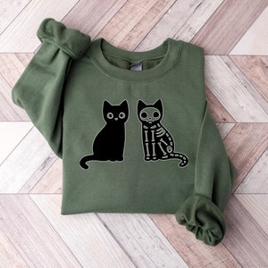May include: A green sweatshirt with a black cat and a skeleton cat graphic. The cats are facing each other.