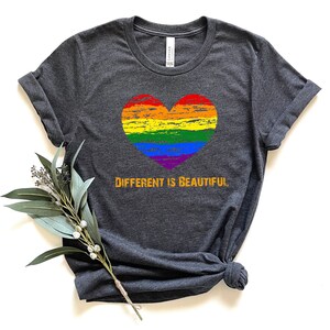 May include: A dark heather grey t-shirt with a rainbow heart and the text "DIFFERENT IS BEAUTIFUL" in orange.