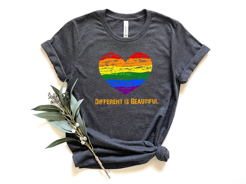 May include: A dark heather grey t-shirt with a rainbow heart and the text "DIFFERENT IS BEAUTIFUL" in orange.