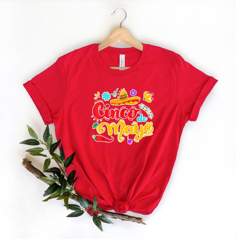 May include: Red t-shirt with a colorful graphic design that says "Cinco de Mayo" with a sombrero and flowers.