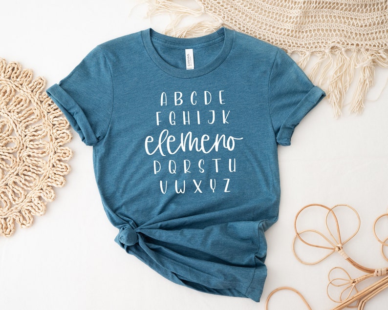 以下が含まれることがあります： 白文字で「ABCDE FGHIJK elemeno PQRTSTU VWXYZ」と書かれたターコイズブルーのTシャツです。