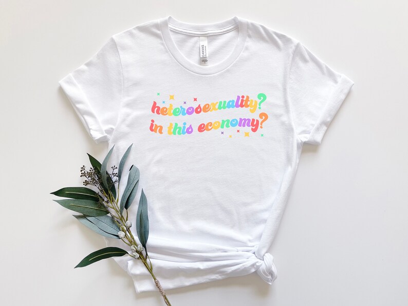 Pu&ograve; includere: Maglietta bianca con la scritta "eterosessualit&agrave;? in questa economia?" stampata in colori arcobaleno.