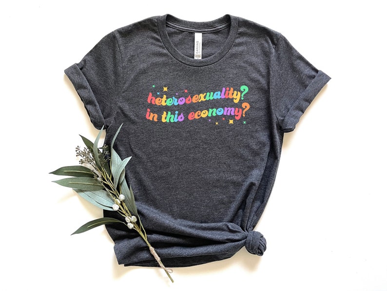 Pu&ograve; includere: Una maglietta grigio scuro con la scritta "eterosessualit&agrave;? in questa economia?" stampata in colori arcobaleno.