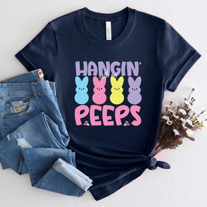 May include: A navy blue t-shirt with the text "Hangin' with my Peeps" in pink and white lettering. Four colorful marshmallow peeps are arranged in a row above the text.