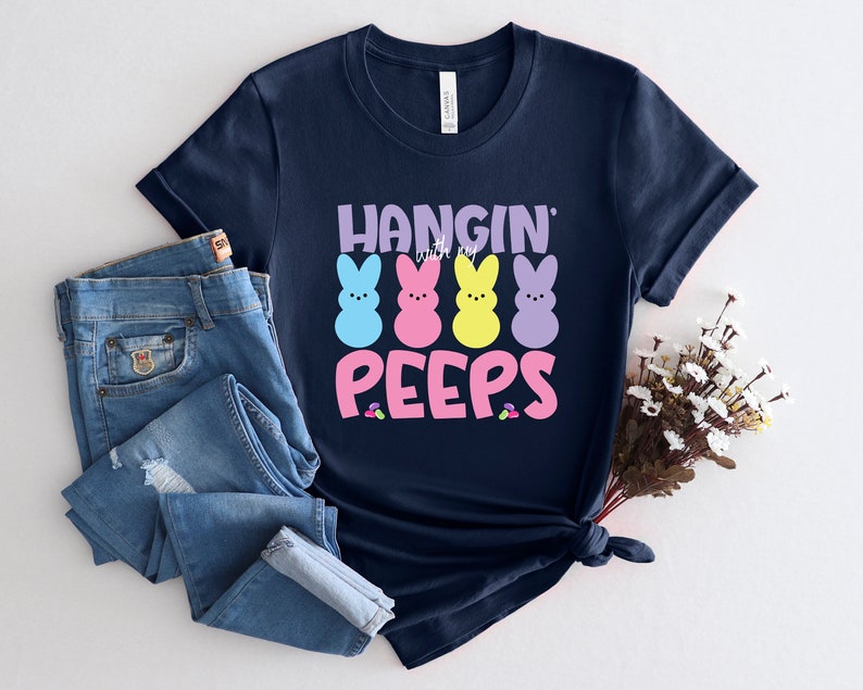 May include: A navy blue t-shirt with the text "Hangin' with my Peeps" in pink and white lettering. Four colorful marshmallow peeps are arranged in a row above the text.