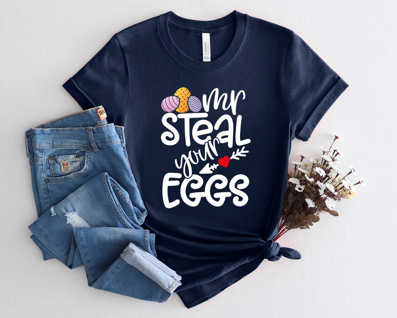 May include: A navy blue t-shirt with a white graphic that says "I'm steal your eggs" with a heart and arrow. The graphic also includes a cluster of colourful Easter eggs.