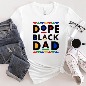 K&ouml;nnte beinhalten: Wei&szlig;es T-Shirt mit einem grafischen Design, das "Dope Black Dad" in schwarzen und gelben Buchstaben mit einem bunten geometrischen Muster um den Text herum sagt.