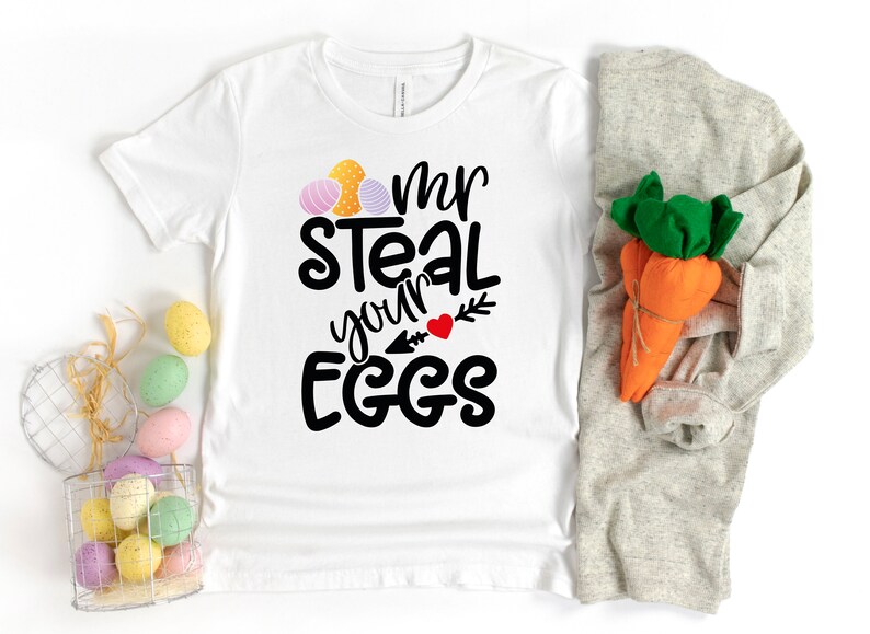 May include: White t-shirt with black text that reads "Mr Steal your Eggs" with a red heart and arrow. The shirt is decorated with three colourful Easter eggs.