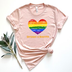 May include: A light pink t-shirt with a rainbow heart and the text "DIFFERENT IS BEAUTIFUL" in orange.