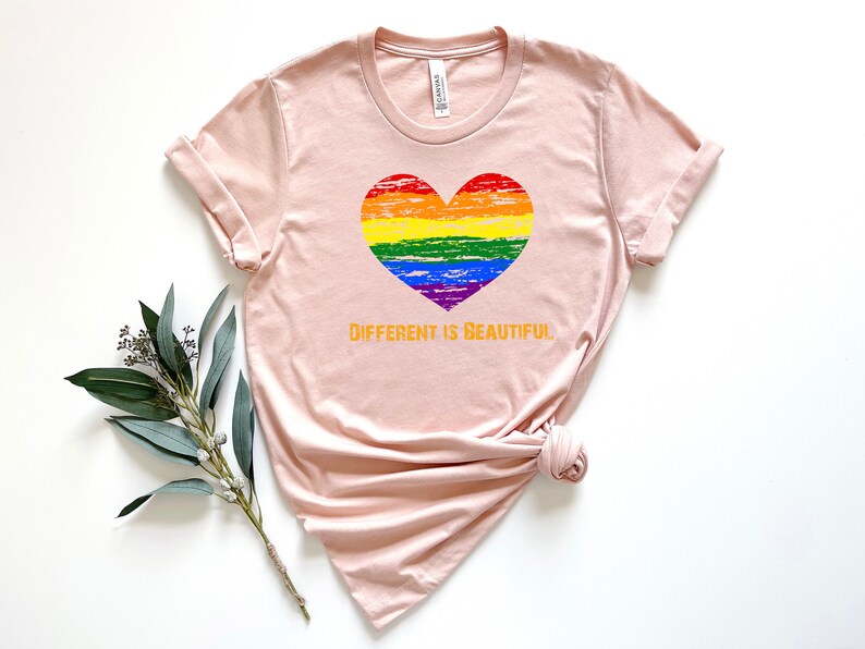 May include: A light pink t-shirt with a rainbow heart and the text "DIFFERENT IS BEAUTIFUL" in orange.