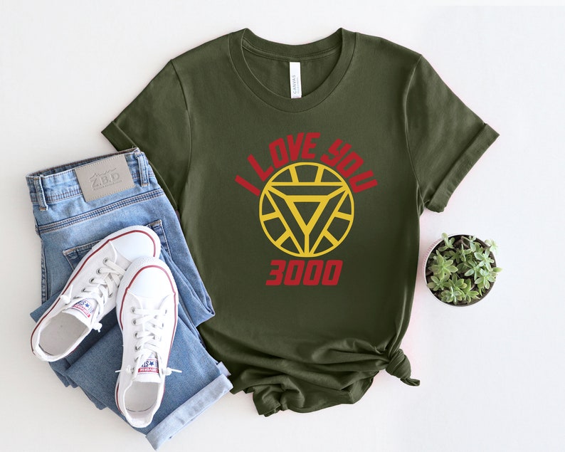 Puede incluir: Una camiseta verde con un logotipo de Iron Man rojo y amarillo y el texto "I love you 3000".