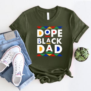 K&ouml;nnte beinhalten: Ein gr&uuml;nes T-Shirt mit einer wei&szlig;en Grafik, auf der "Dope Black Dad" im Retro-Stil mit bunten geometrischen Formen steht.