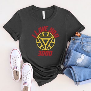 Puede incluir: Una camiseta gris oscuro con un gr&aacute;fico rojo y amarillo de la m&aacute;scara de Iron Man y el texto "I Love You 3000".