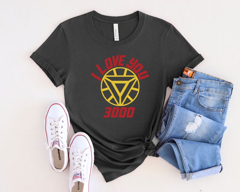 Puede incluir: Una camiseta gris oscuro con un gr&aacute;fico rojo y amarillo de la m&aacute;scara de Iron Man y el texto "I Love You 3000".