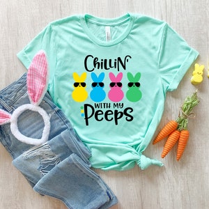 May include: A turquoise blue t-shirt with the text "Chillin' with my Peeps" and a graphic of four colorful marshmallow peeps wearing sunglasses.