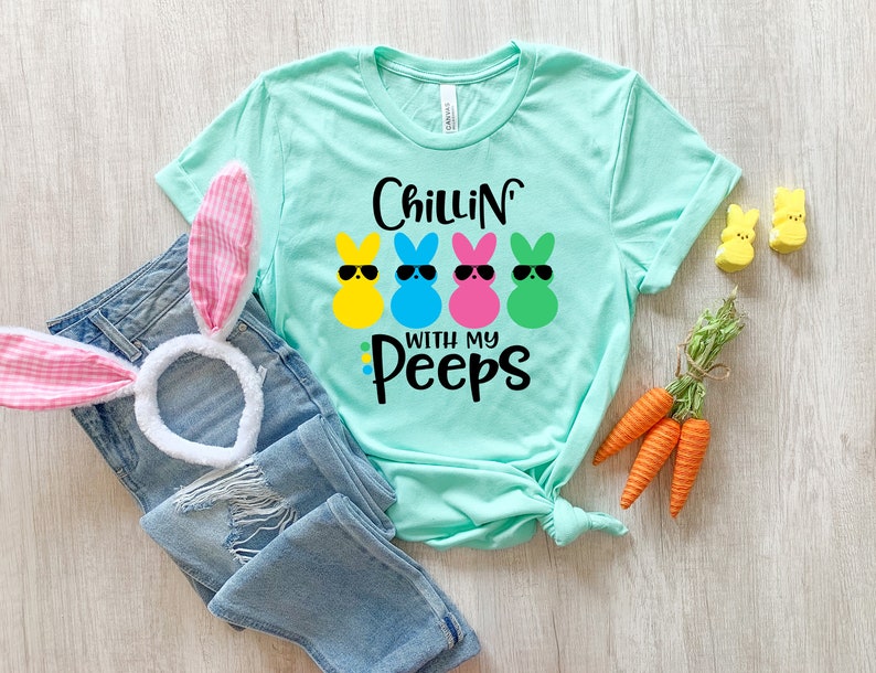 May include: A turquoise blue t-shirt with the text "Chillin' with my Peeps" and a graphic of four colorful marshmallow peeps wearing sunglasses.