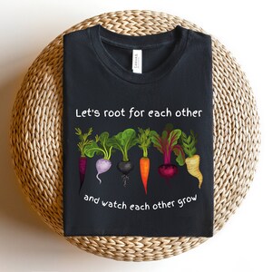 May include: Black t-shirt with a white graphic of five colorful vegetables with the text "Let's root for each other and watch each other grow".
