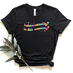 Pu&ograve; includere: Maglietta nera con testo arcobaleno che recita "eterosessualit&agrave;? in questa economia?"