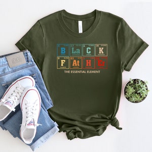 Puede incluir: Una camiseta verde con un gr&aacute;fico de la tabla peri&oacute;dica de los elementos que deletrea "BLACK" y "F*CKER" con el texto "THE ESSENTIAL ELEMENT" debajo.