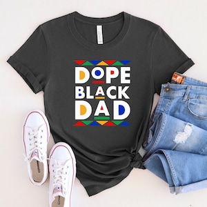 K&ouml;nnte beinhalten: Ein dunkelgraues T-Shirt mit dem Text "Dope Black Dad" in bunten Blockbuchstaben. Die Buchstaben sind schwarz umrandet und haben ein geometrisches Muster dahinter.
