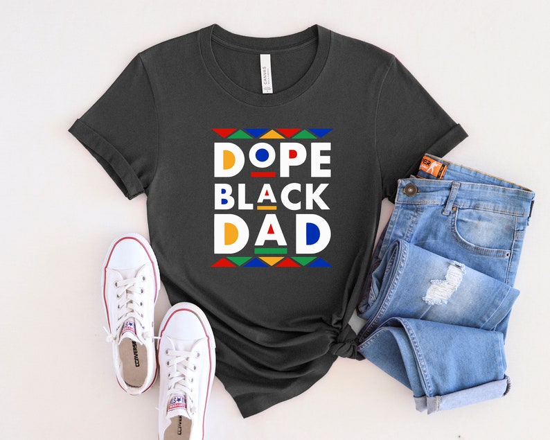 K&ouml;nnte beinhalten: Ein dunkelgraues T-Shirt mit dem Text "Dope Black Dad" in bunten Blockbuchstaben. Die Buchstaben sind schwarz umrandet und haben ein geometrisches Muster dahinter.