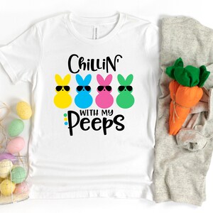 May include: White t-shirt with the text "Chillin' with my Peeps" and four cartoon Peeps wearing sunglasses. The Peeps are yellow, blue, pink, and green.