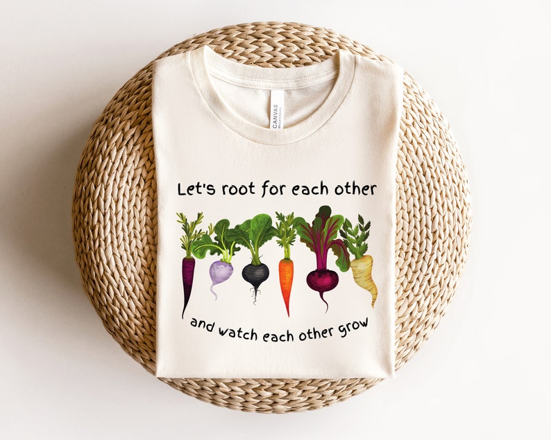 May include: A white t-shirt with a graphic of colorful root vegetables and the text "Let's root for each other and watch each other grow".