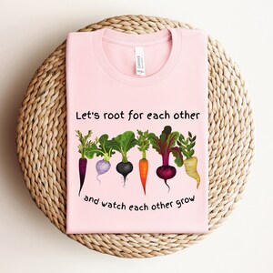 May include: Pink t-shirt with a graphic of five different vegetables with roots and the text "Let's root for each other and watch each other grow".