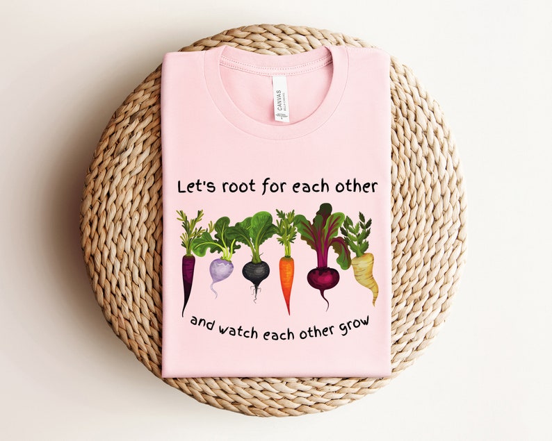 May include: Pink t-shirt with a graphic of five different vegetables with roots and the text "Let's root for each other and watch each other grow".