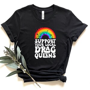 May include: Black t-shirt with a rainbow and the text "Support Your Local Drag Queens" in white.