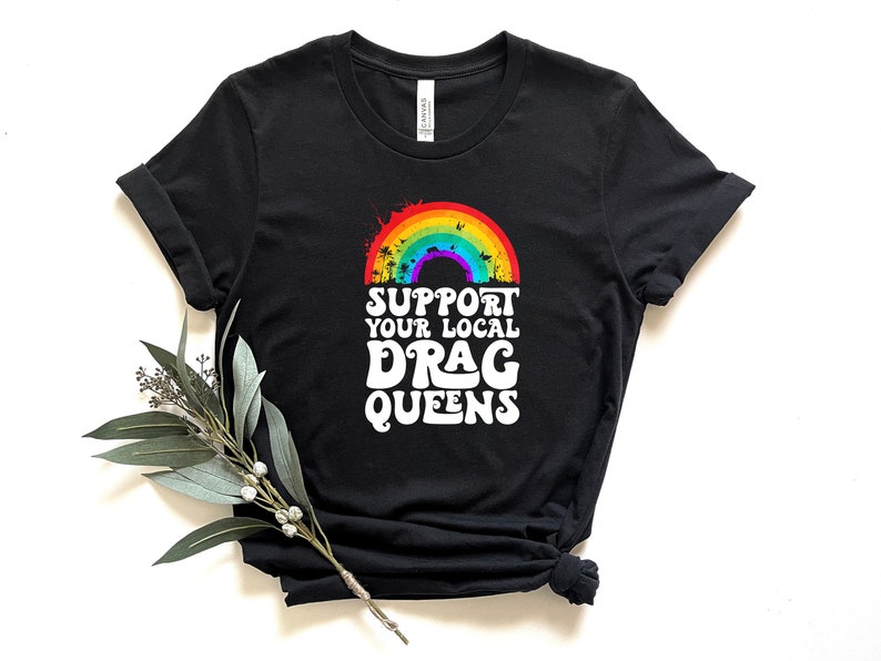 May include: Black t-shirt with a rainbow and the text "Support Your Local Drag Queens" in white.