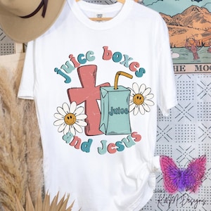 May include: White t-shirt with a graphic design of a cross, a juice box, and daisies. The text "juice boxes and Jesus" is written in a retro font.