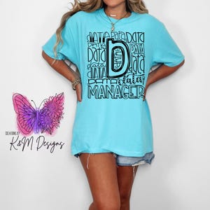 May include: A turquoise blue t-shirt with a black graphic design that says "Data Manager" with the letter "D" being large and surrounded by the word "data" repeated in different styles.