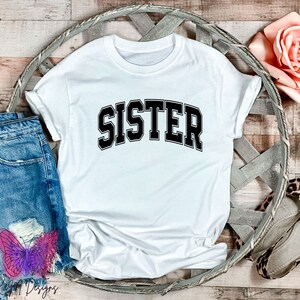 May include: White t-shirt with black text that reads "SISTER" in a collegiate font.