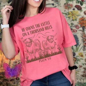 May include: Pink t-shirt with a brown graphic of two Highland cows and the text "He owns the cattle on a thousand hills Psalm 50".
